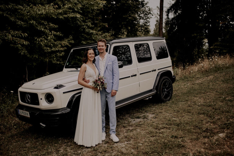 Andrea und Dieter stehen gemeinsam vor der weißen Mercedes-Benz G-Klasse nach der Hochzeit