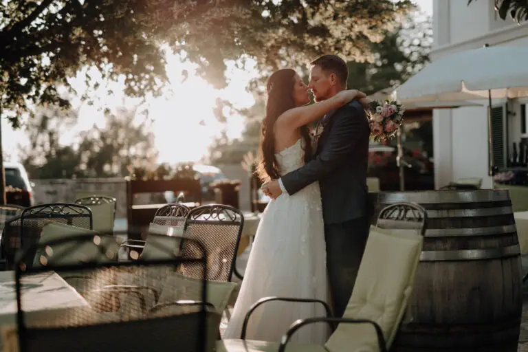 Brautpaar steht bei Sonnenuntergang im Gegenlicht auf der Terrasse des Berggasthof König